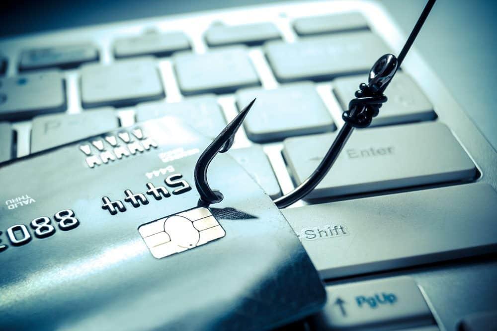 **Alt text (in Italian):**  
Carta di credito agganciata da un amo su tastiera: pericolo phishing online.