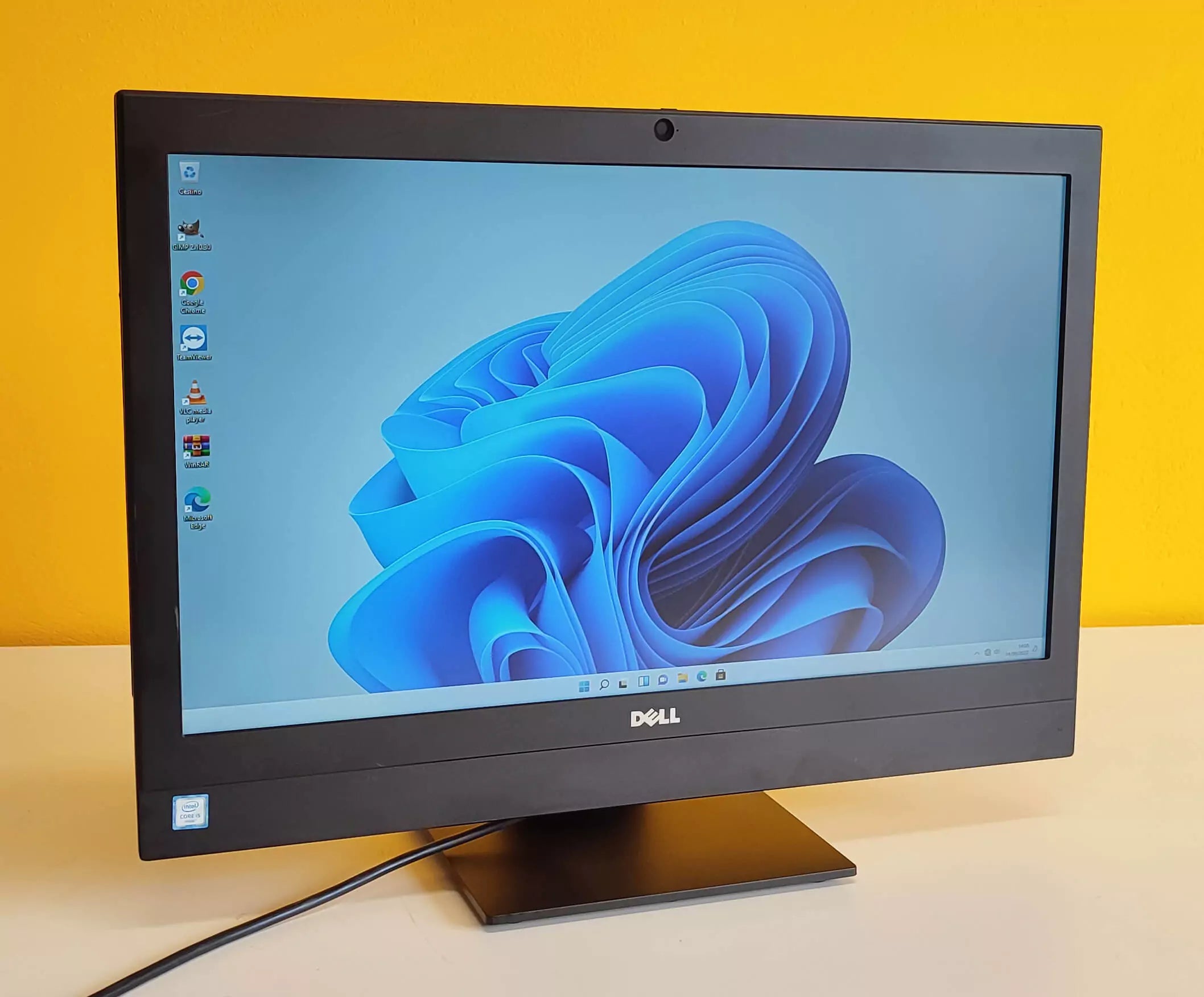 PC All-in-One Dell 7440 ricondizionato su scrivania con sfondo giallo, Windows 11 aperto.